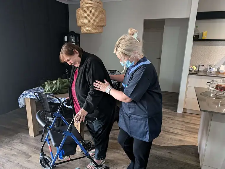 Healthcare professional assisting a woman with a walker indoors